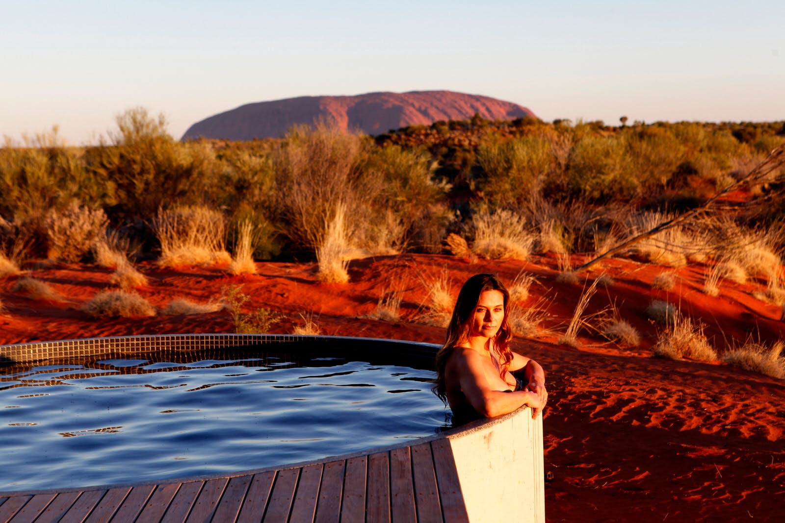 Features - glamping-uluru-2204f6065937 A woman sits in a hot tub with Australia's Uluru in the background.